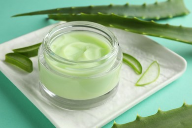 Photo of Jar of natural cream and aloe leaves on green background, closeup