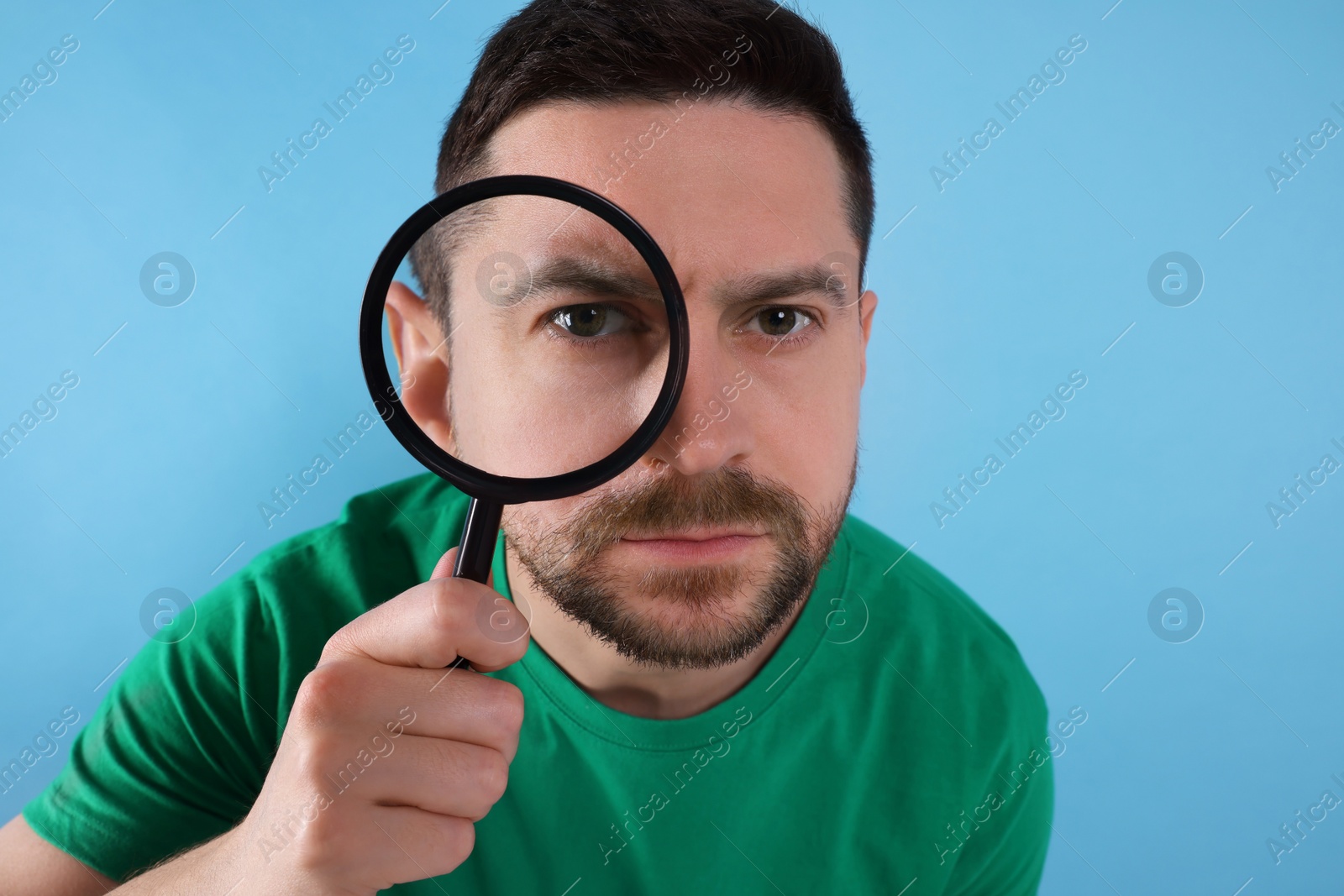 Photo of Man looking through magnifier glass on light blue background