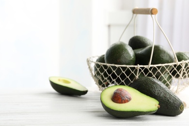 Photo of Delicious ripe avocados on white wooden table against light background