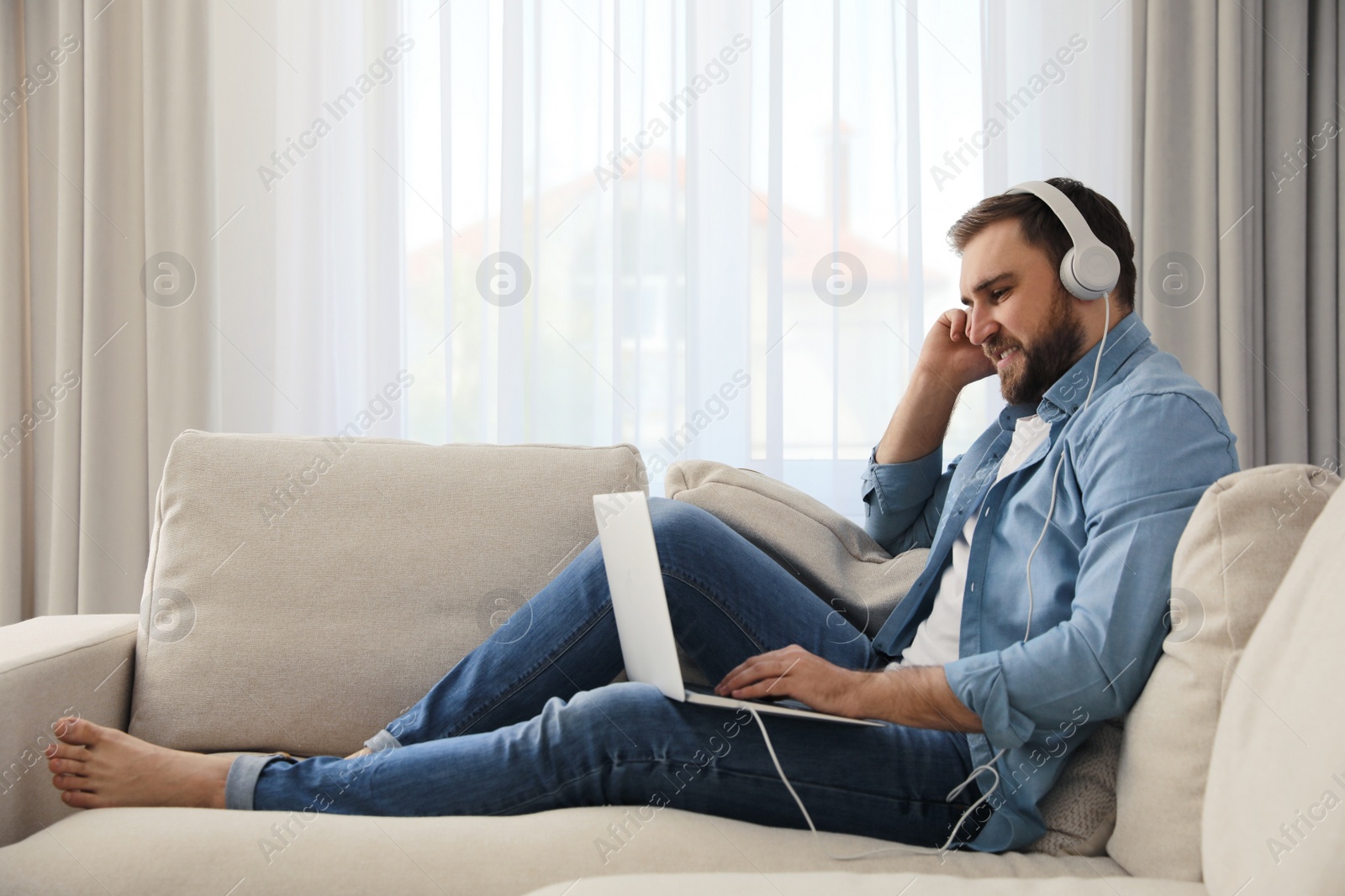 Photo of Man with laptop and headphones sitting on sofa at home