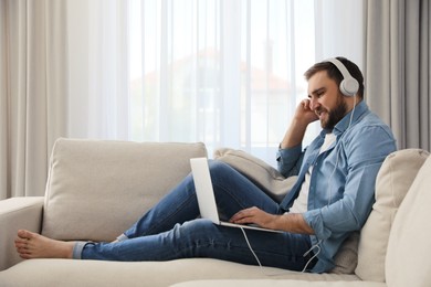 Photo of Man with laptop and headphones sitting on sofa at home