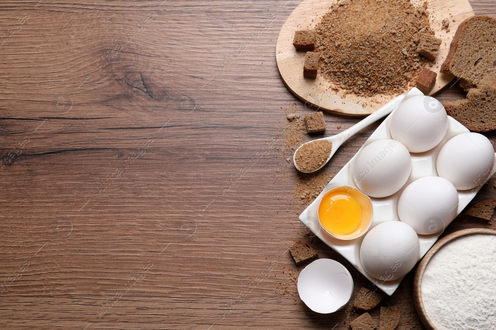 Photo of Fresh breadcrumbs, flour and eggs on wooden table, flat lay. Space for text