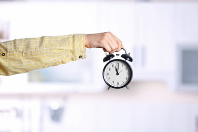 Photo of Young woman holding alarm clock on blurred background. Time concept