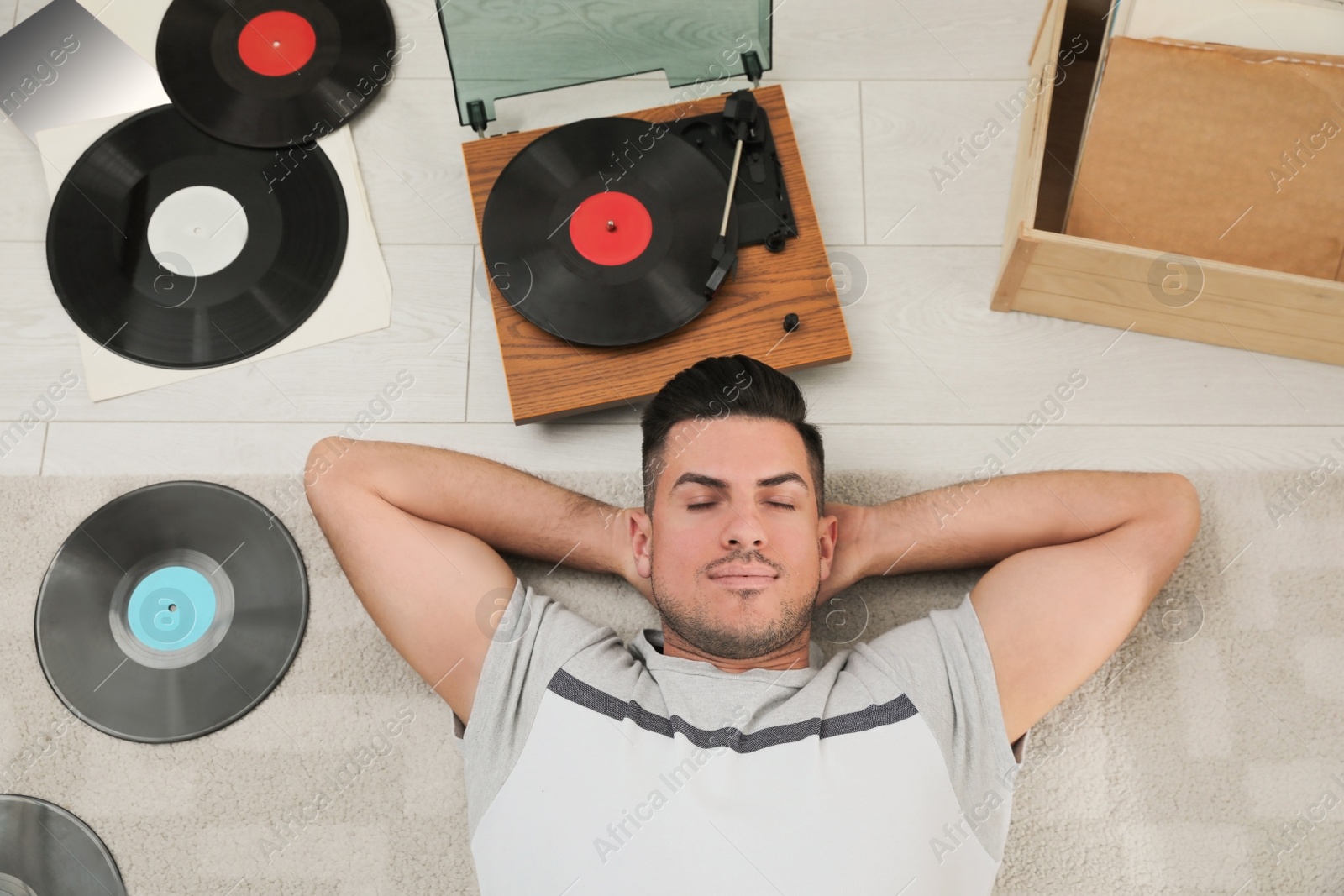 Photo of Man listening to music with turntable while lying on floor at home, above view