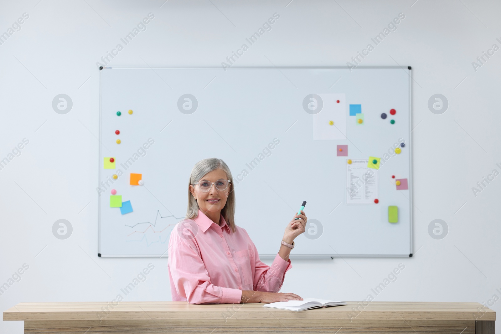 Photo of Professor with marker giving lecture at desk in classroom