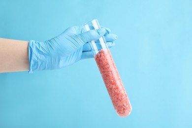 Photo of Scientist holding test tube with minced lab grown meat on light blue background, closeup