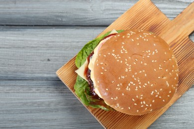 Photo of Tasty homemade cheeseburger with lettuce on grey wooden table, top view. Space for text