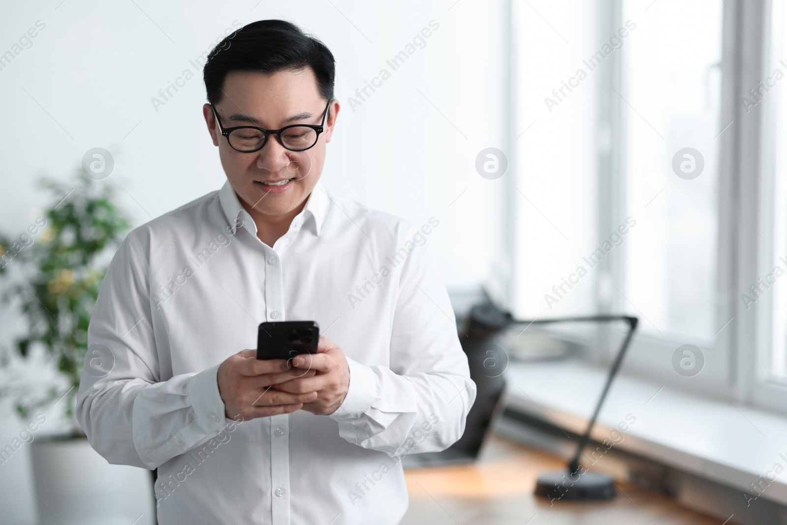 Photo of Portrait of smiling businessman with smartphone in office. Space for text