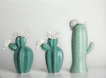 Trendy cactus shaped vases with flowers on table against light wall. Creative decor