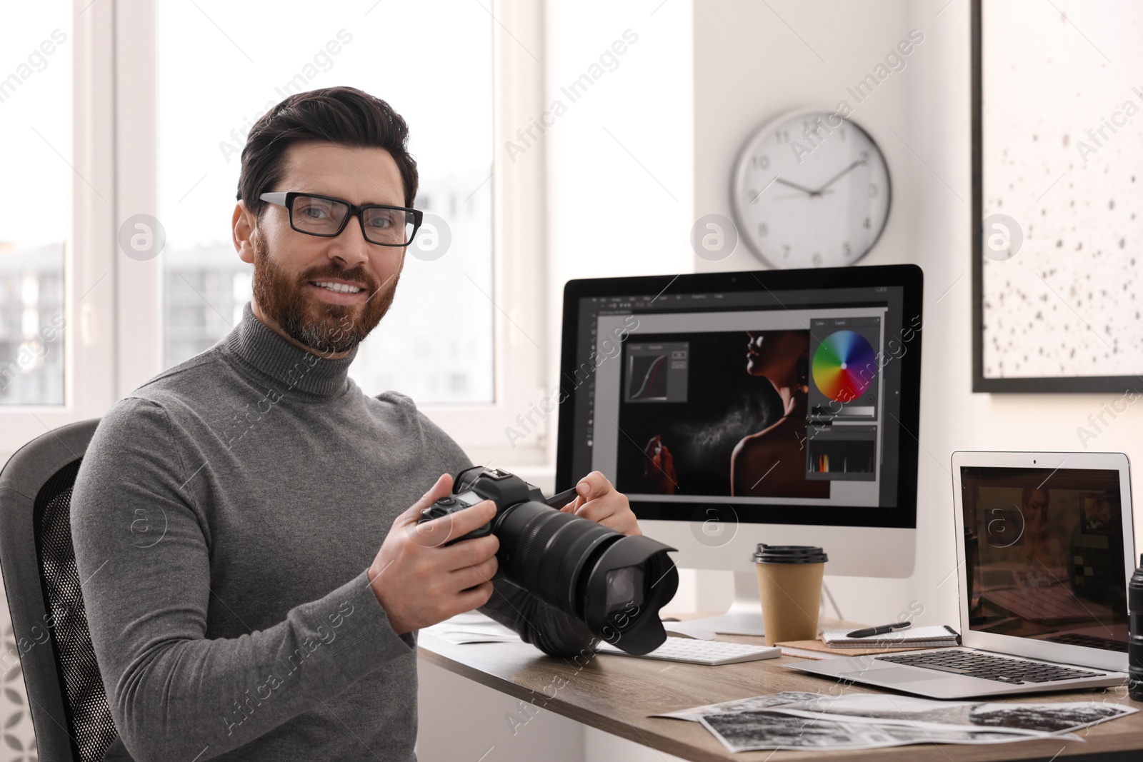 Photo of Professional photographer in glasses holding digital camera at table in office