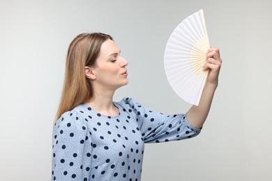 Photo of Beautiful woman waving hand fan to cool herself on light grey background