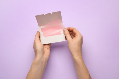 Woman with package of oil blotting tissues on violet background, top view. Mattifying wipes