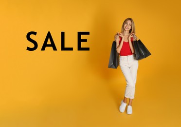 Happy young woman with shopping bags and word SALE on yellow background