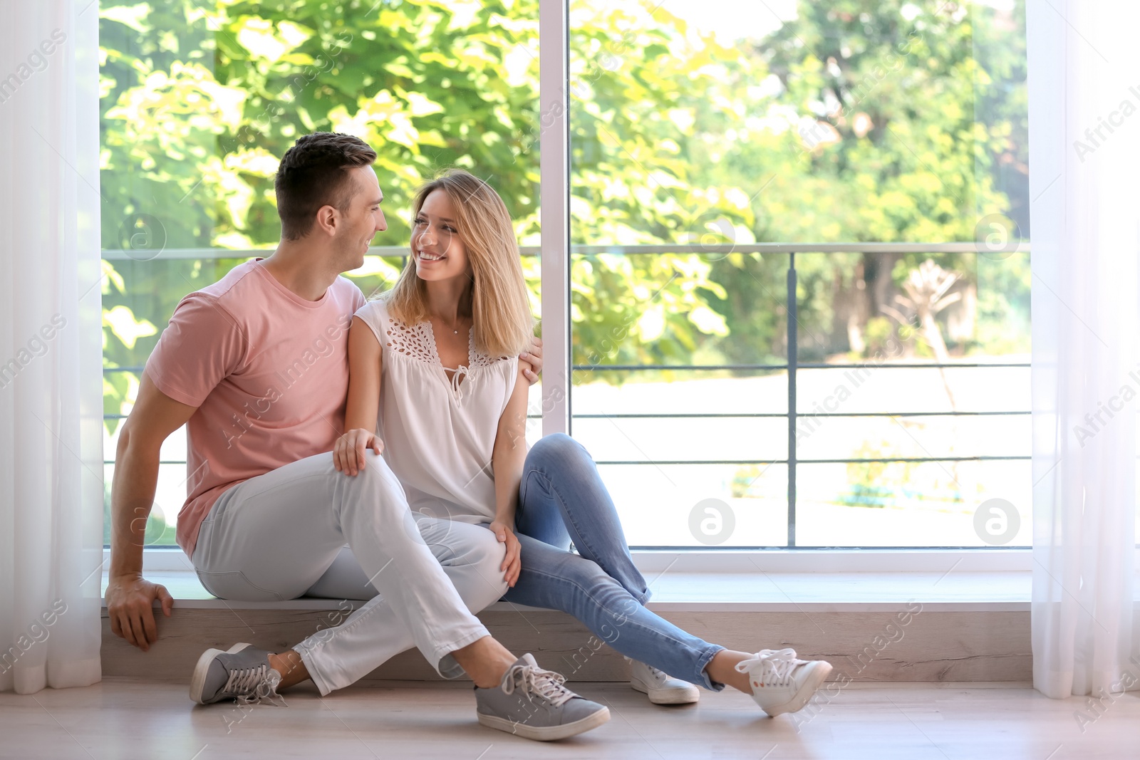 Photo of Happy young couple sitting near window at home