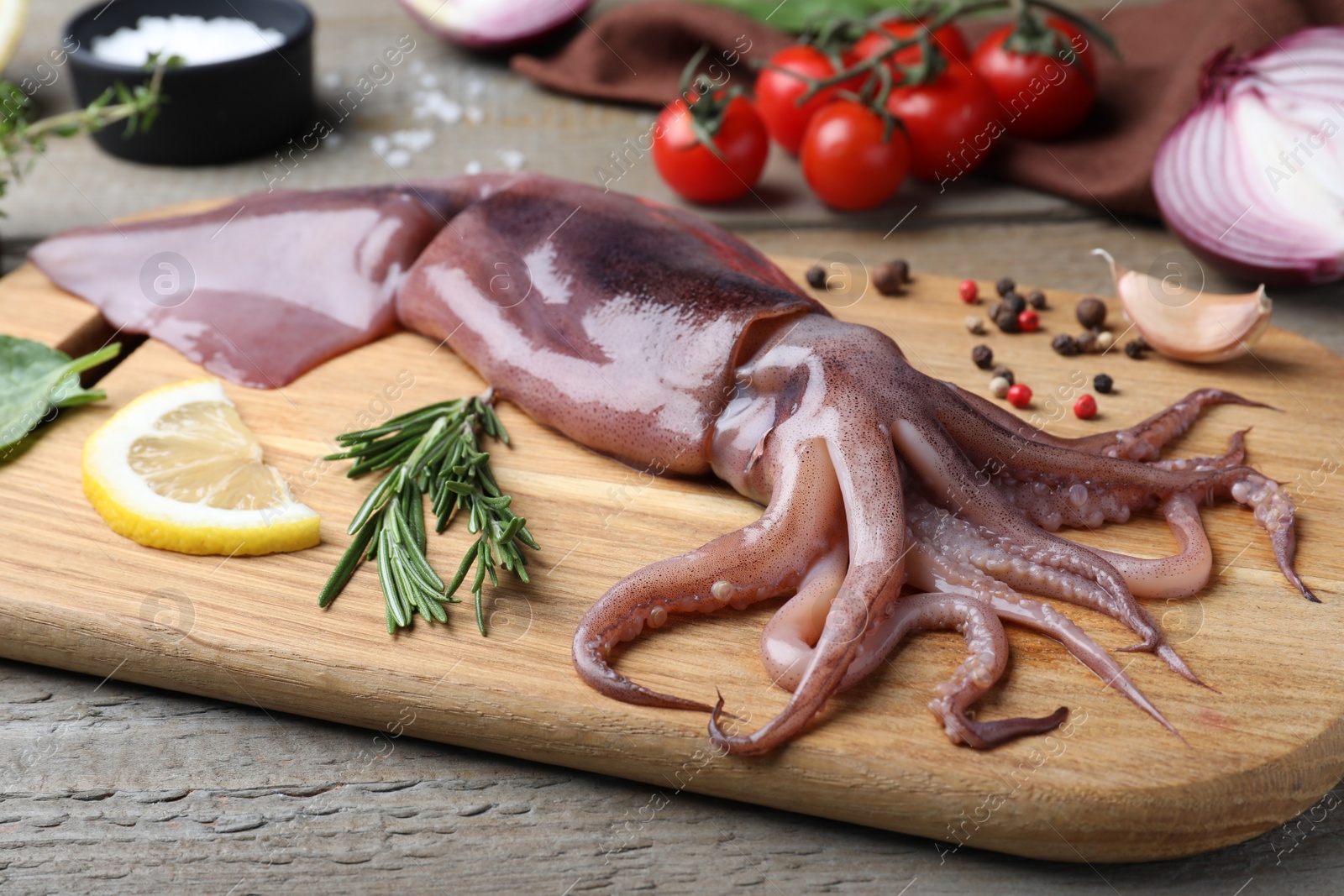 Photo of Fresh raw squid with lemon, rosemary and pepper on wooden table, closeup