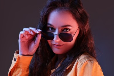 Photo of Portrait of beautiful young woman with stylish sunglasses on color background with neon lights