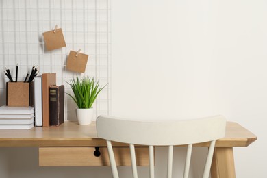 Comfortable workplace with wooden desk near white wall. Space for text