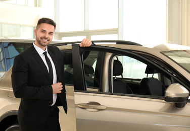 Young salesman near new car in dealership