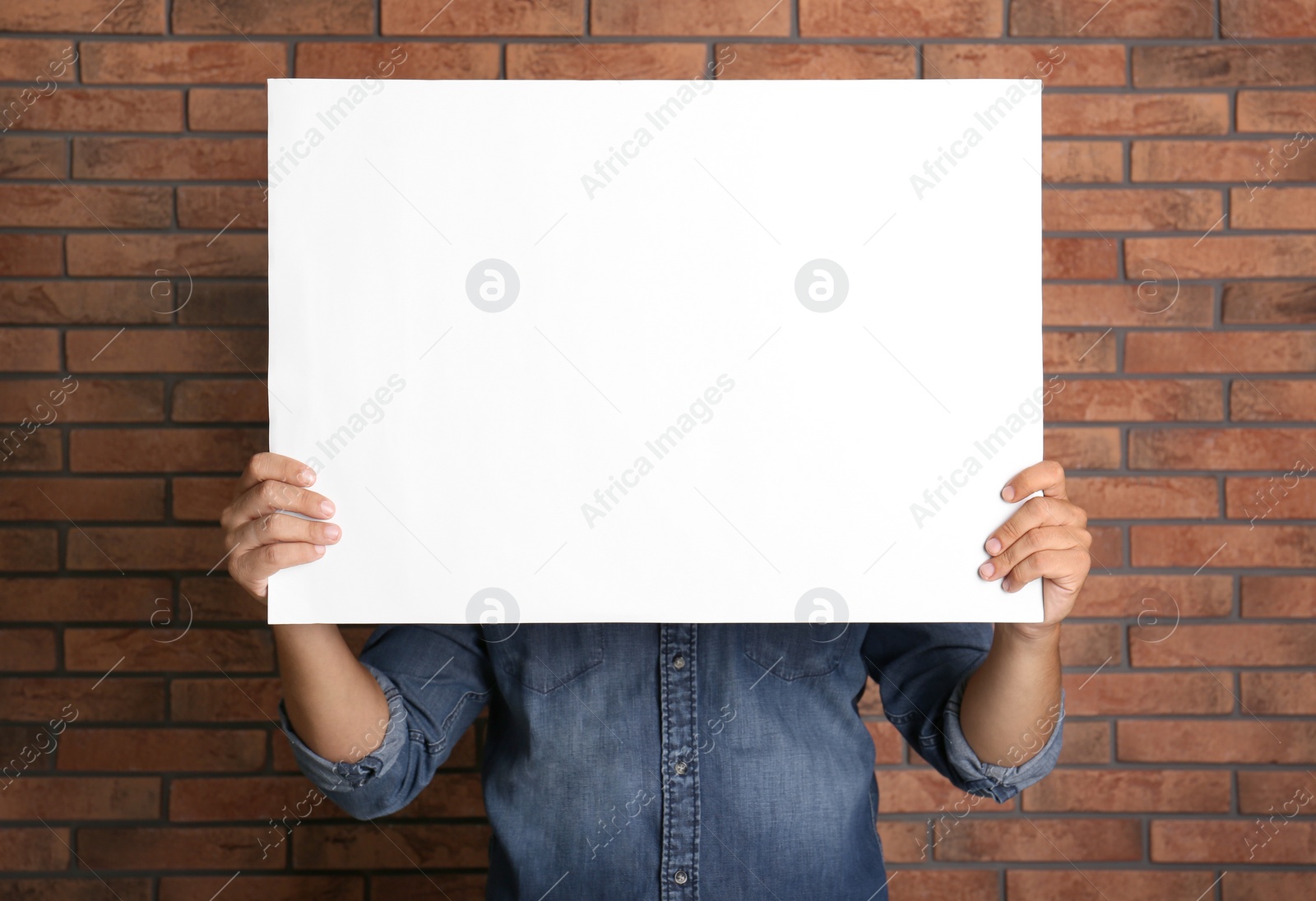 Photo of Man holding white blank poster near red brick wall. Mockup for design