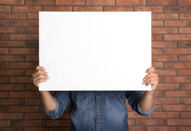 Photo of Man holding white blank poster near red brick wall. Mockup for design