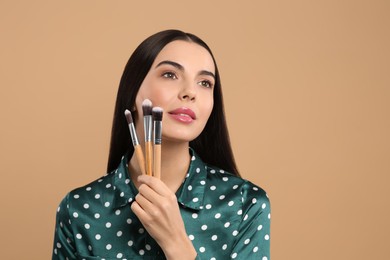 Photo of Beautiful woman with different makeup brushes on light brown background. Space for text
