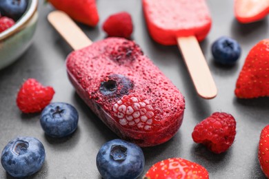 Photo of Tasty berry ice pops on dark table, closeup. Fruit popsicle