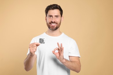 Photo of Man with condom showing ok gesture on beige background. Safe sex