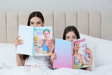 Young mother and her daughter with magazines on bed at home