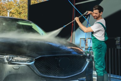 Worker washing auto with high pressure water jet at outdoor car wash