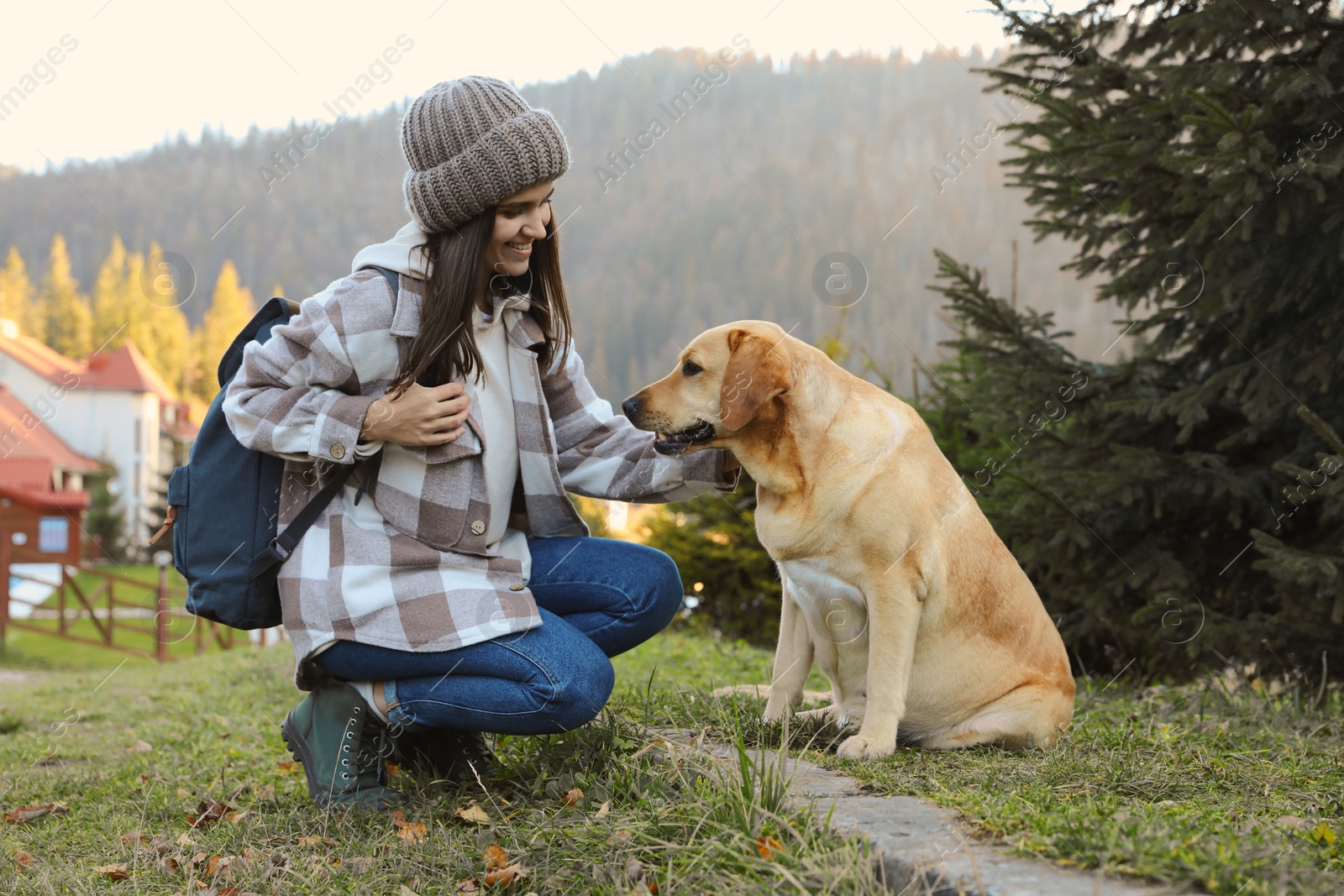 Photo of Happy woman and adorable dog sitting on green grass in mountains. Traveling with pet