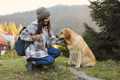 Photo of Happy woman and adorable dog sitting on green grass in mountains. Traveling with pet