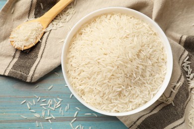 Photo of Raw basmati rice in bowl and spoon on light blue wooden table, top view