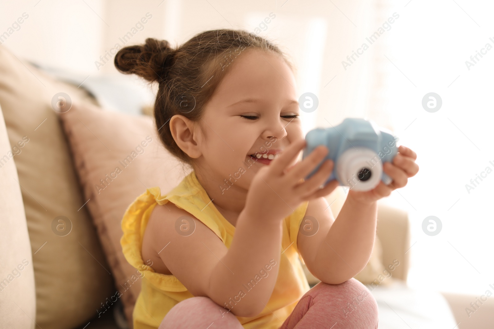 Photo of Little photographer with toy camera on sofa at home