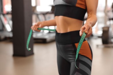 Photo of Slim woman measuring waist with tape in gym, closeup