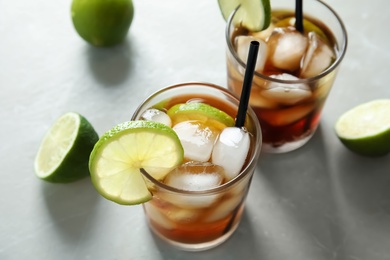 Photo of Glasses of cocktail with cola, ice and cut lime on light background