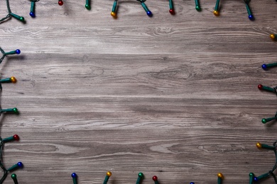 Photo of Frame of Christmas lights on wooden table, top view. Space for text