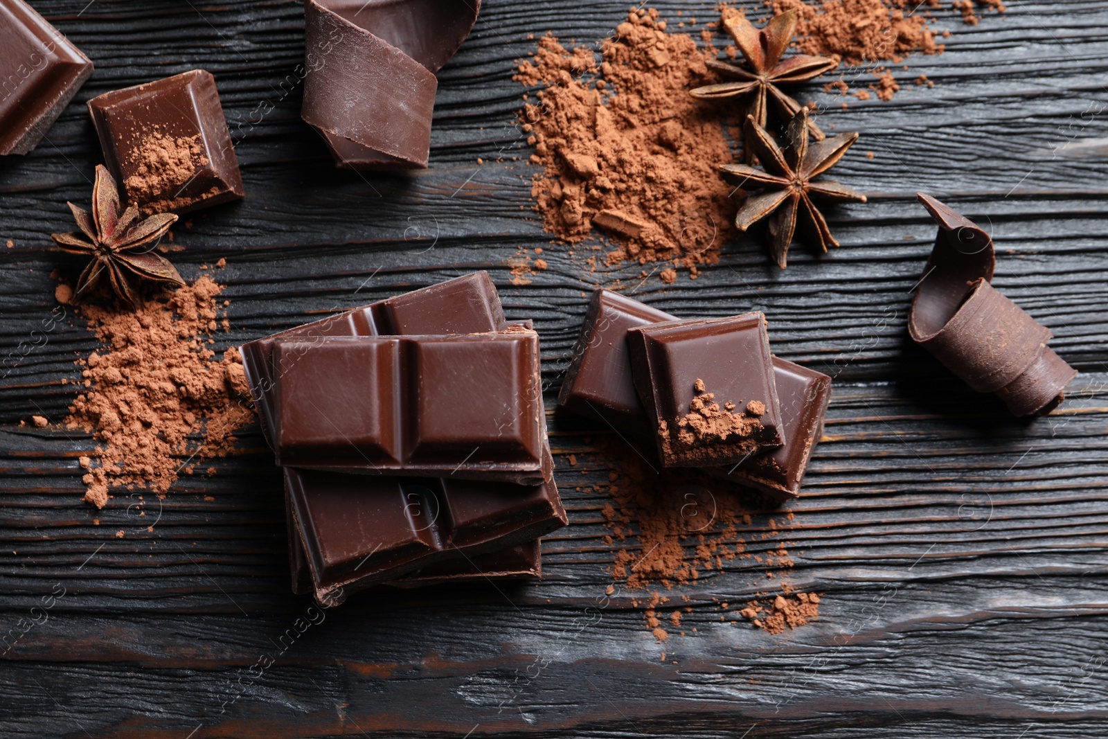 Photo of Pieces of black chocolate on wooden table, flat lay