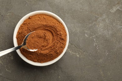 Taking cinnamon powder with spoon from bowl on grey table, top view. Space for text