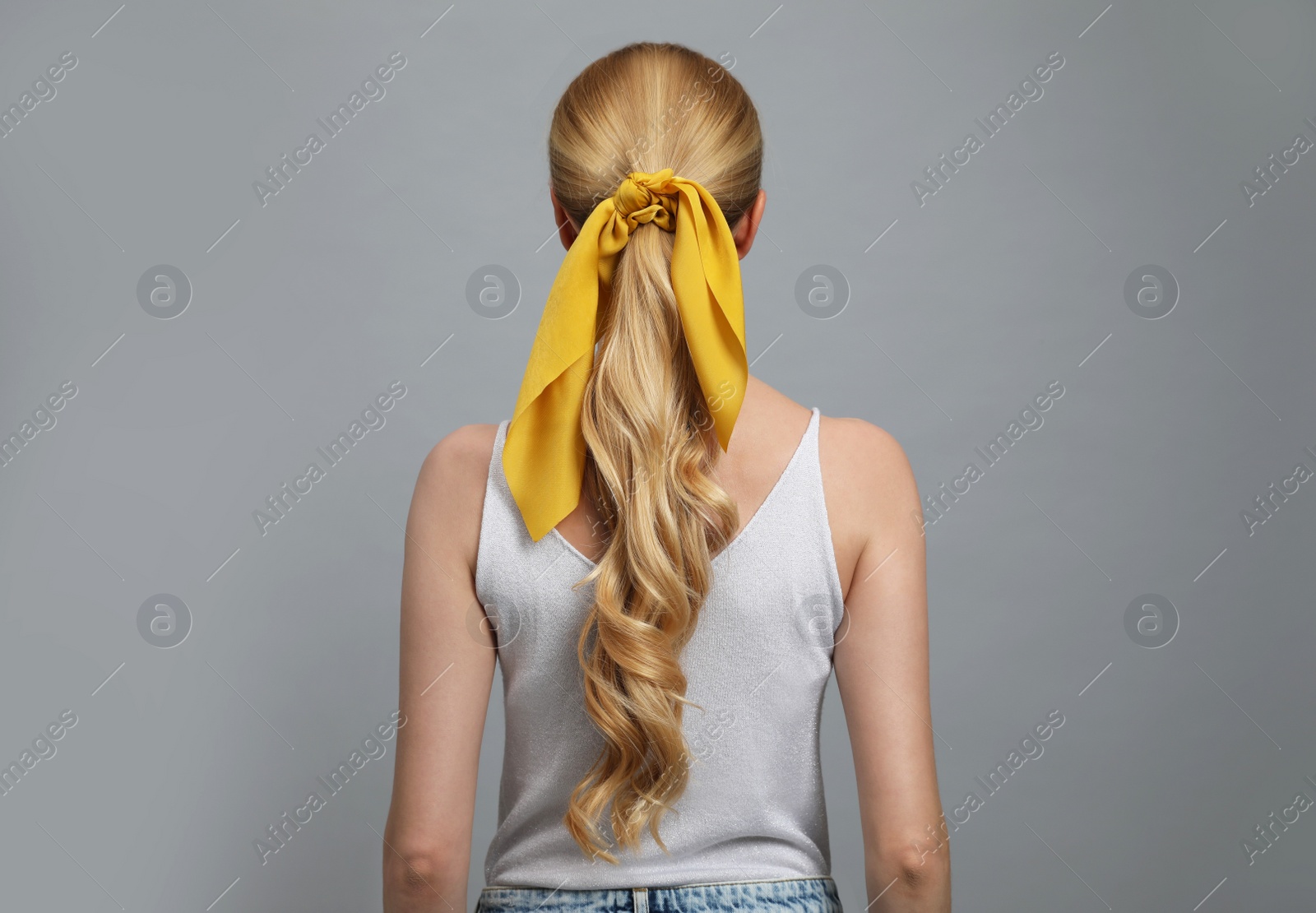 Photo of Young woman with stylish bandana on grey background, back view