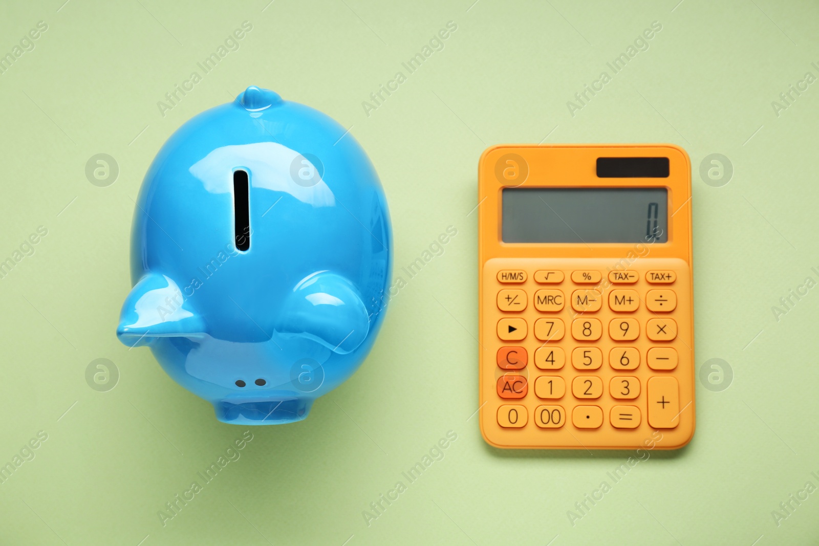 Photo of Piggy bank and calculator on light green background, flat lay