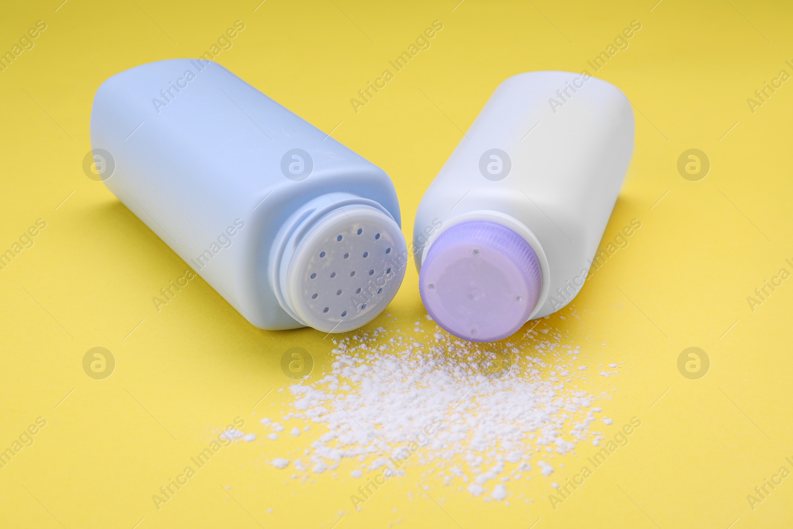 Photo of Bottles and scattered dusting powder on yellow background, closeup. Baby cosmetic products