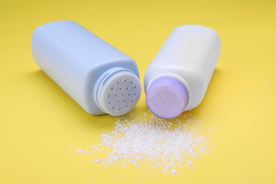 Photo of Bottles and scattered dusting powder on yellow background, closeup. Baby cosmetic products