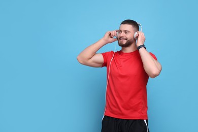 Photo of Handsome man with headphones on light blue background, space for text