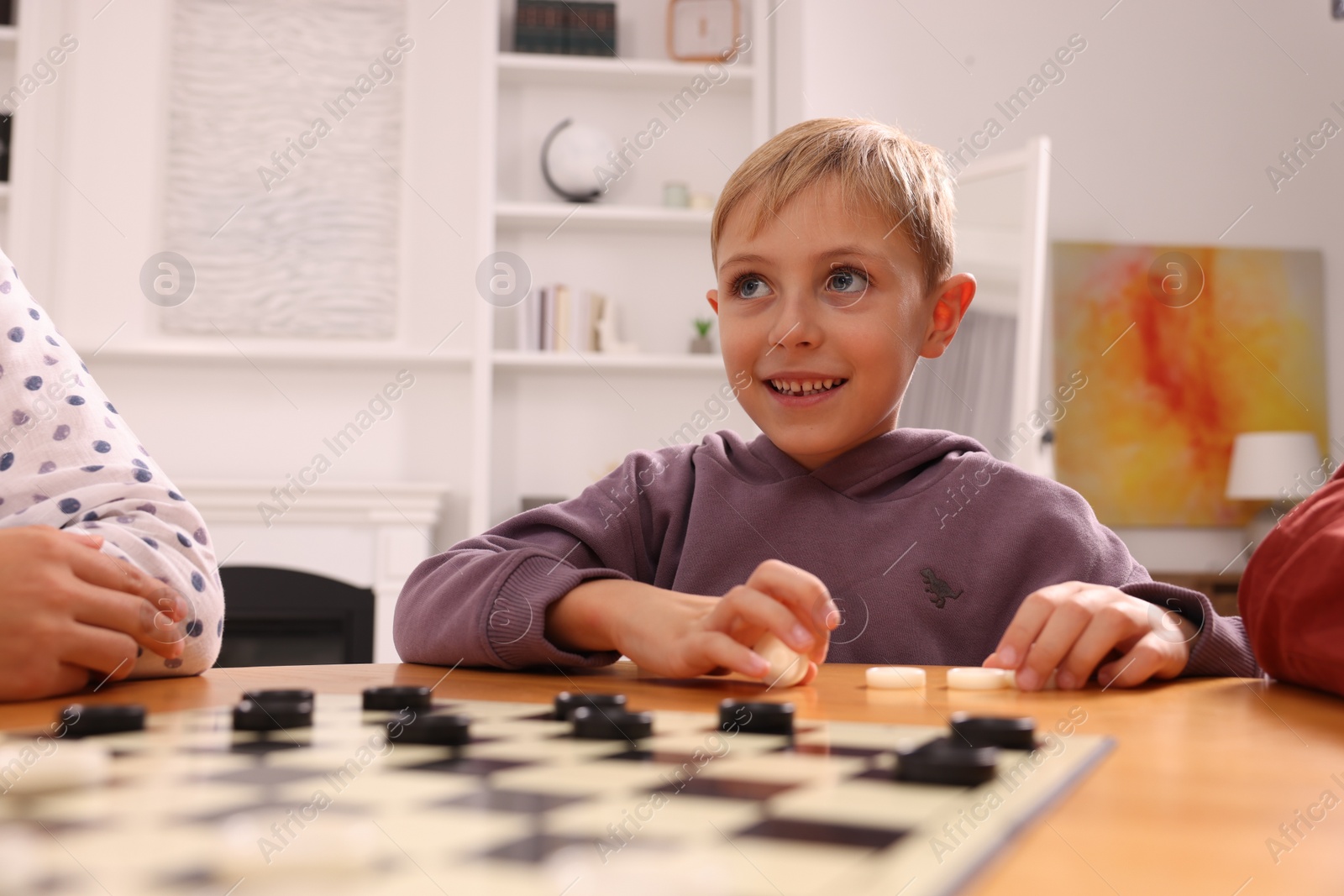 Photo of Boy playing checkers at wooden table in room
