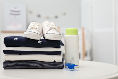 Stack of baby clothes, shoes and accessories on white table indoors