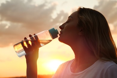 Photo of Young woman drinking water to prevent heat stroke outdoors at sunset