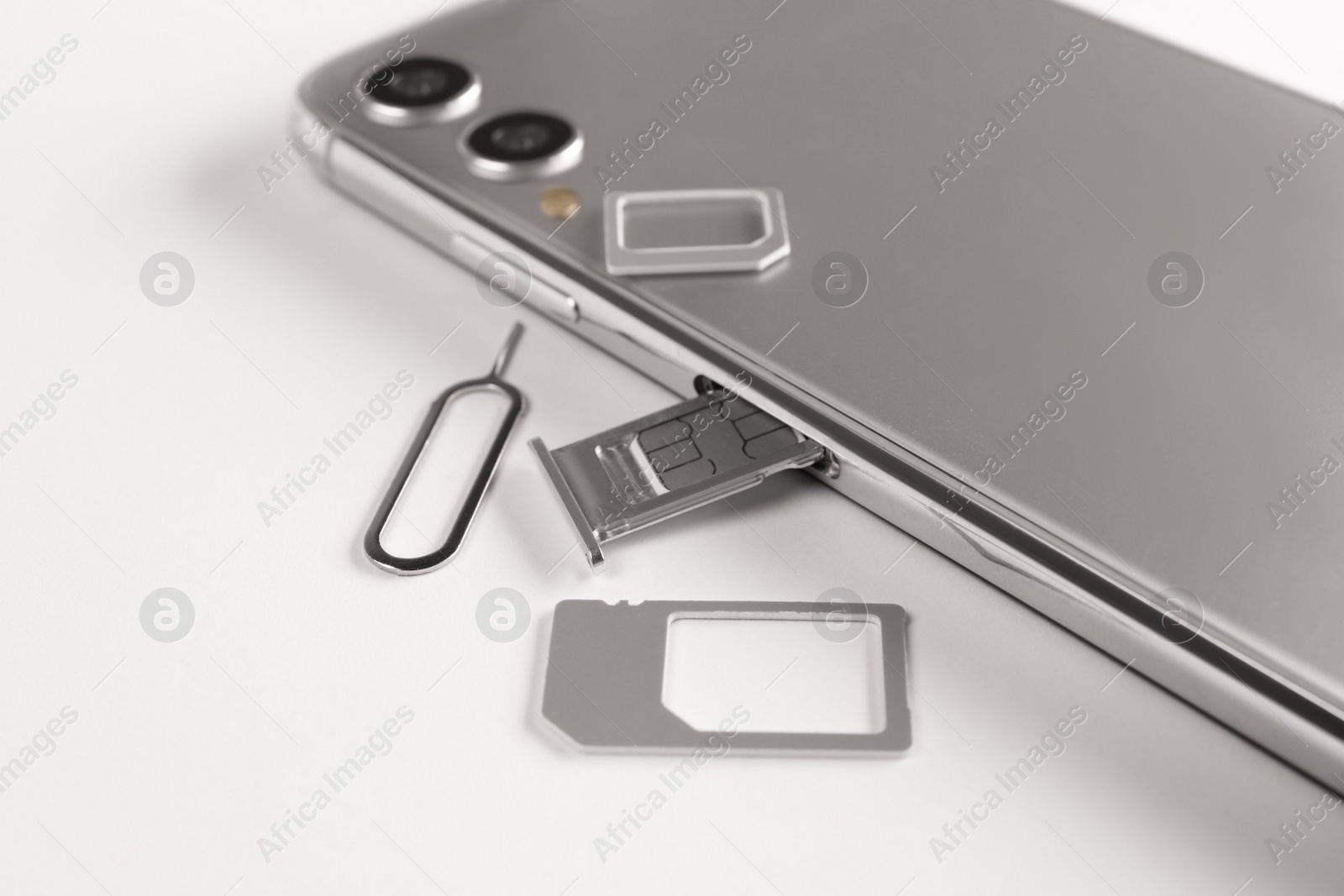 Photo of SIM card, mobile phone and ejector tool on white table
