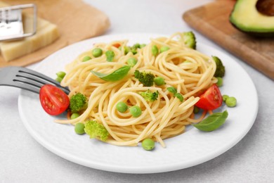 Plate of delicious pasta primavera and ingredients on light gray table, closeup