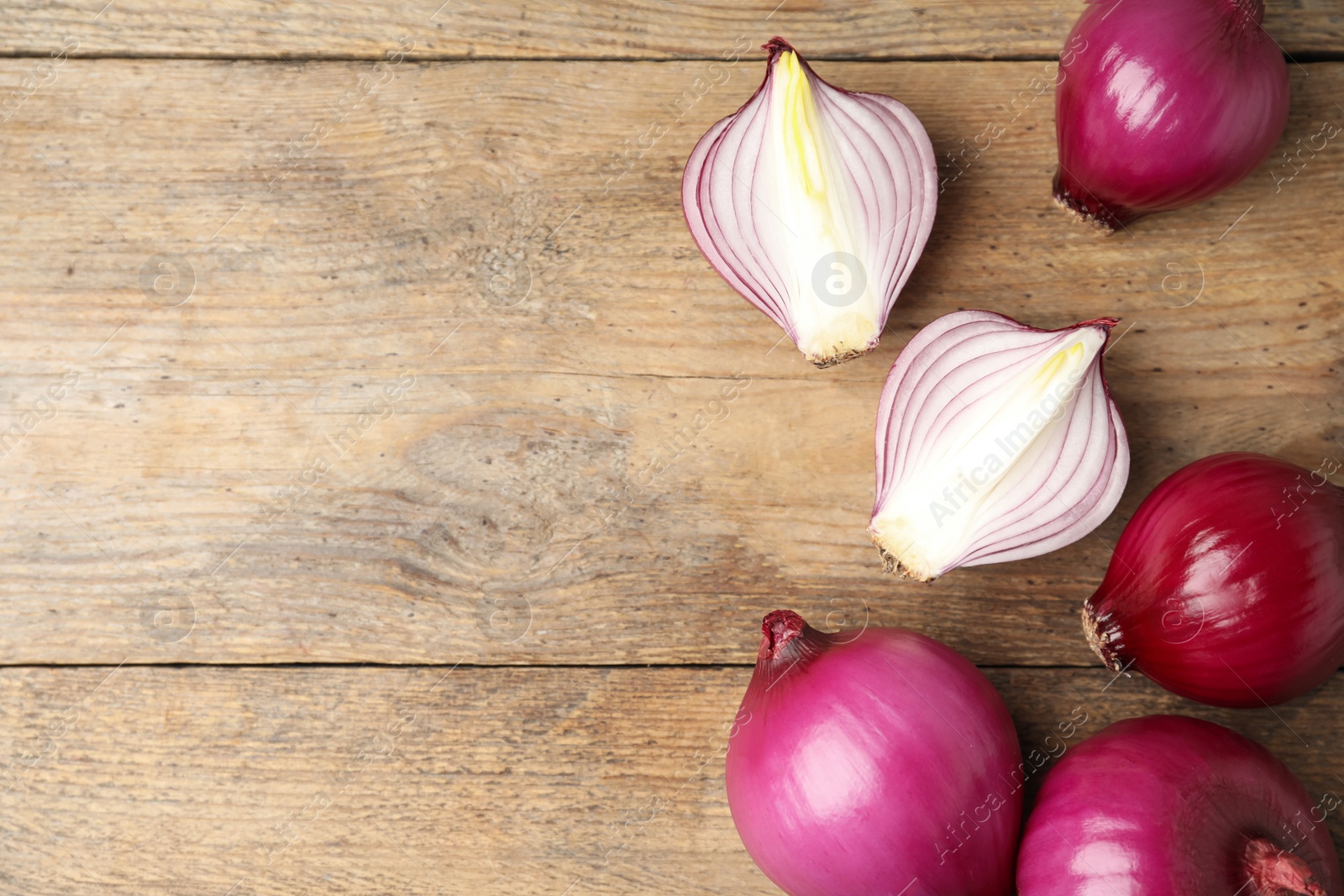 Photo of Ripe red onion bulbs on wooden table, flat lay. Space for text