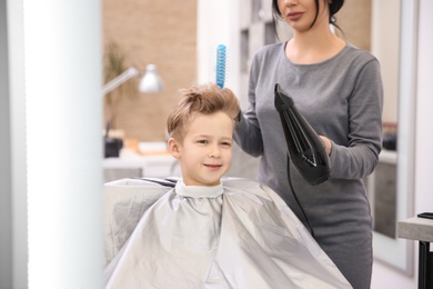 Photo of Professional female hairdresser working with little boy in salon